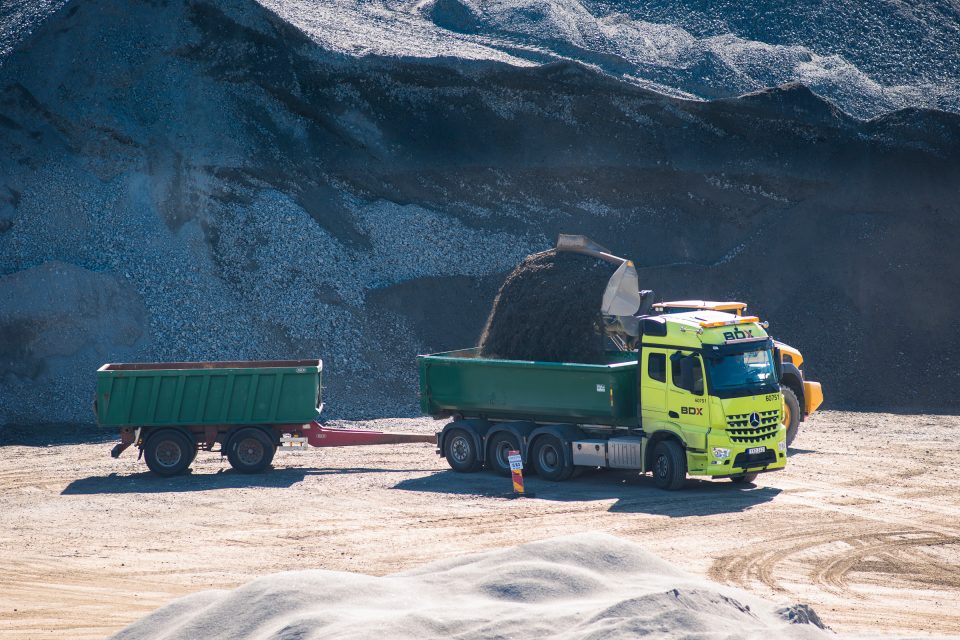 BDX grön lastbil med släp lastas med ballast av hjullastare i bergtäkt